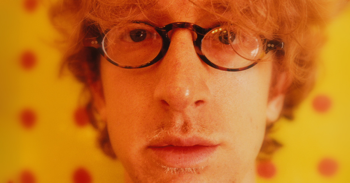 August 10: Andy Dick dressed in an oversized brown sweater and blue striped shirt stands before a painting in his living room on August 10, 1995 in Los Angeles.