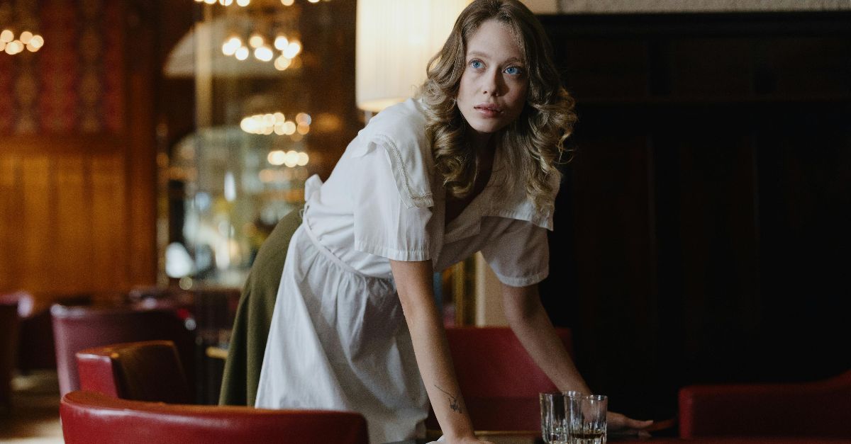 A female waitress wipes a table in a stylish restaurant setting, focused on her task.