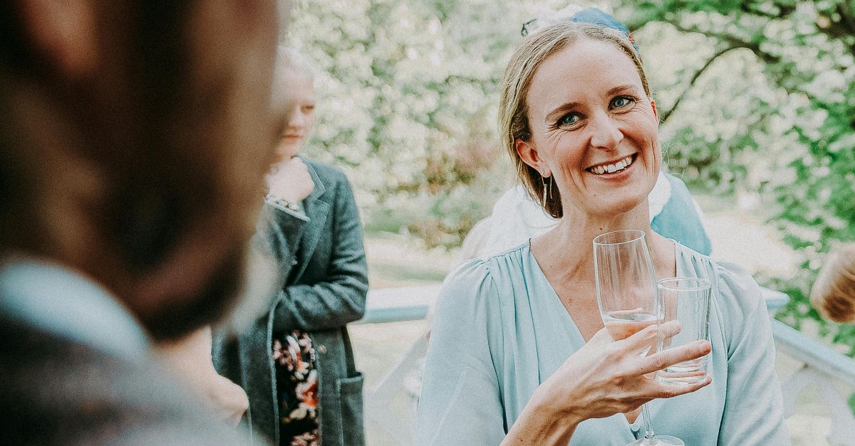 A cheerful woman enjoying a relaxed outdoor gathering with friends, holding a glass drink.