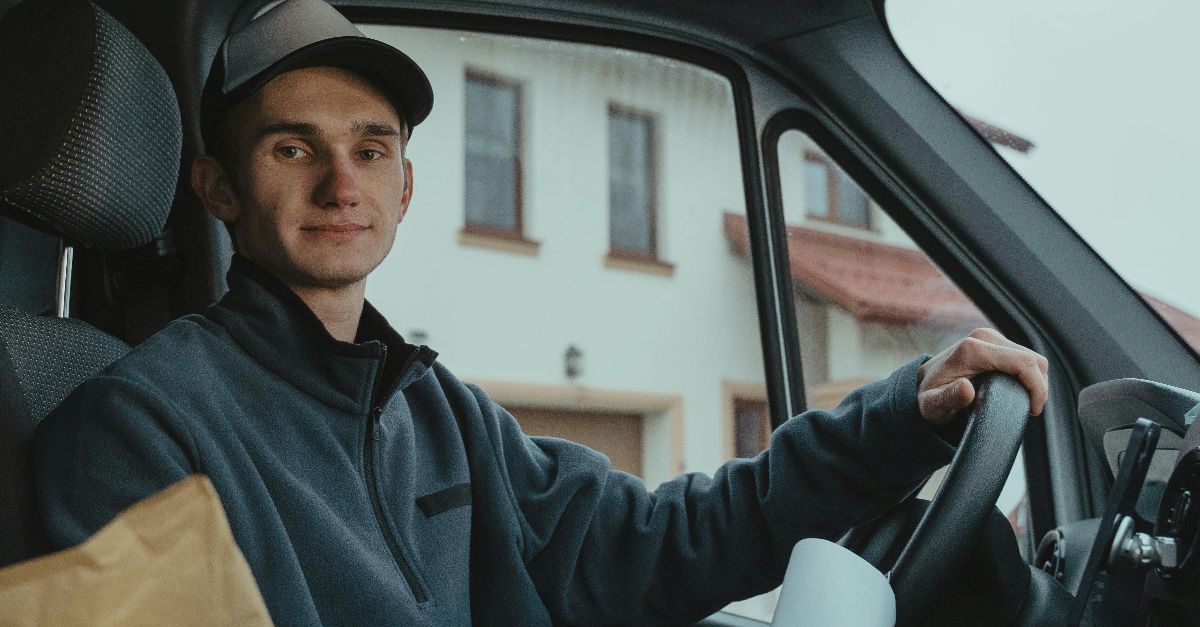 A delivery driver holding documents sits in a van, ready with packages for delivery.