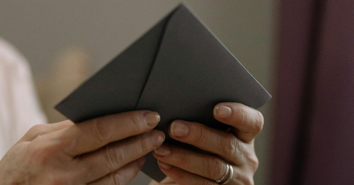 A close-up of a smiling senior woman holding an envelope indoors on a sunny day.
