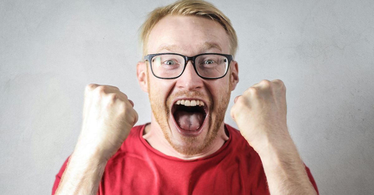 A cheerful man in a red shirt expressing excitement indoors.