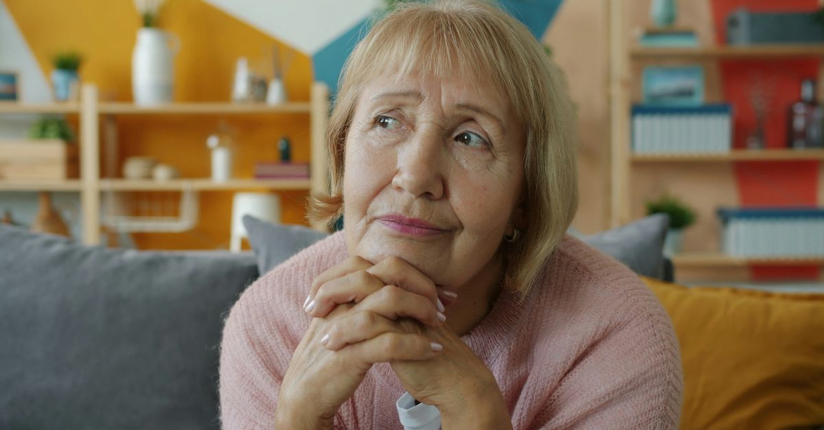 Elderly woman with hands clasped, looking thoughtful.