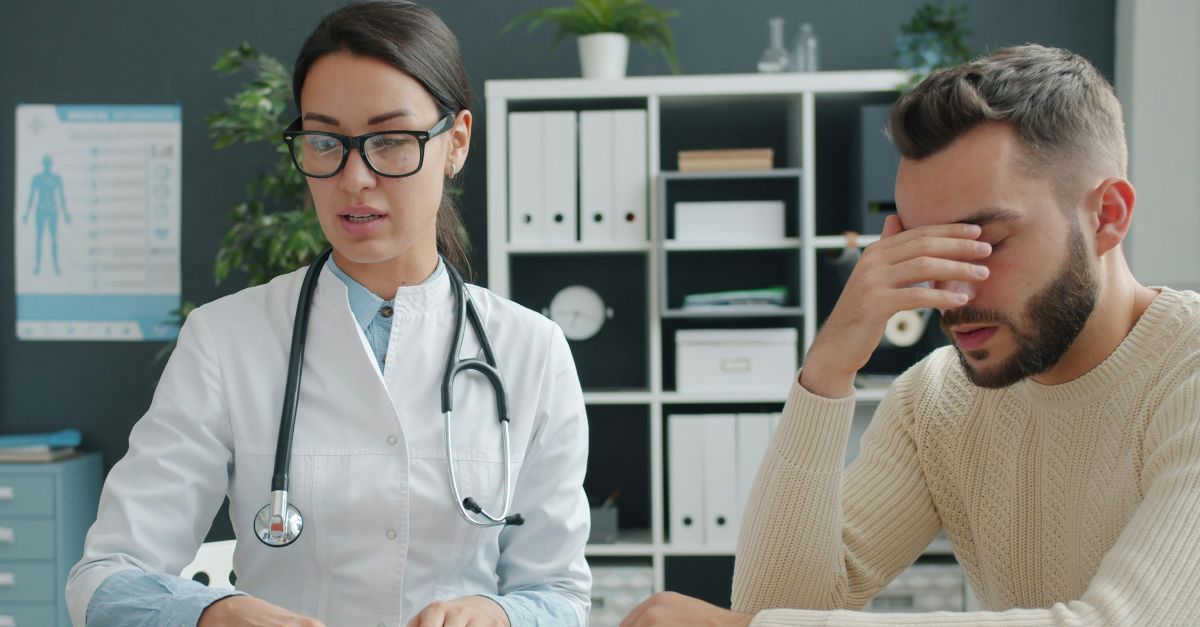 Doctor consults with a distressed male patient in office.