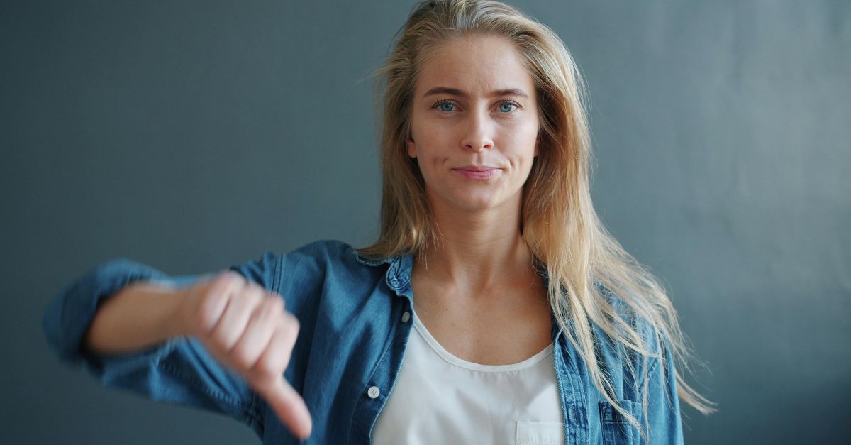 Confident young woman displaying a thumbs down sign against a neutral background.