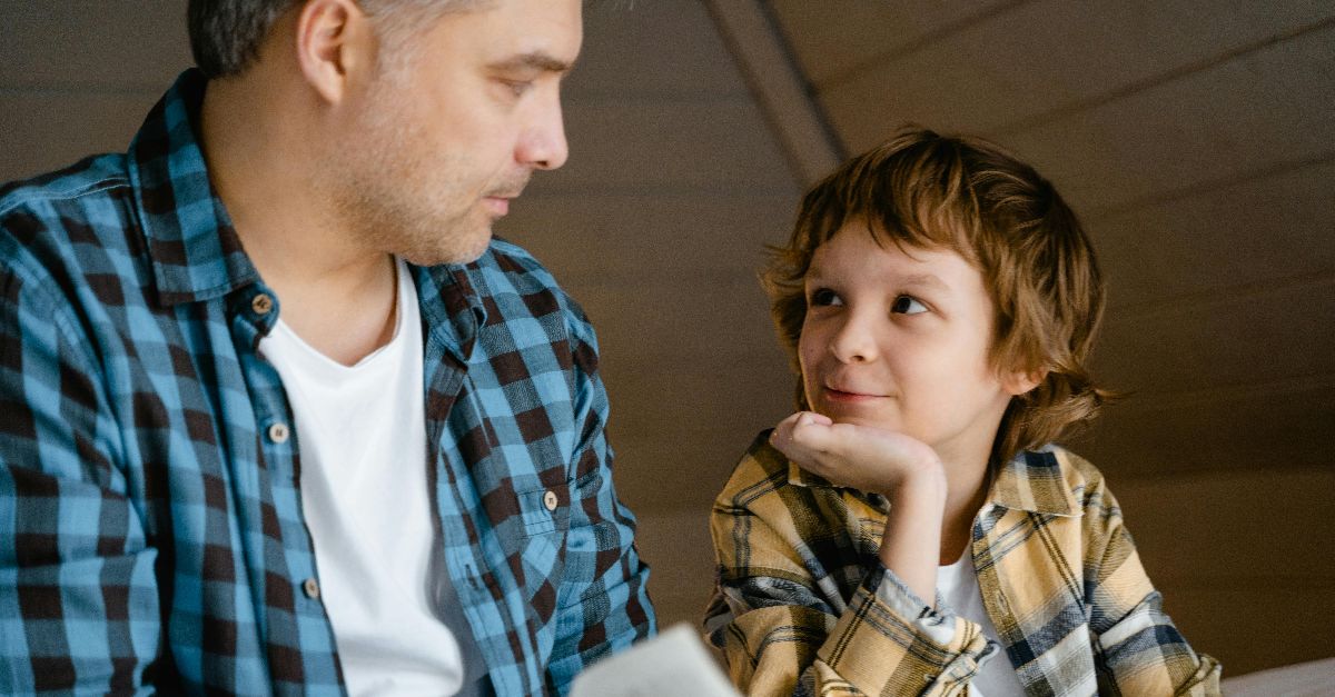 A father and son enjoy a cozy bedtime story together in a warm, indoor setting.