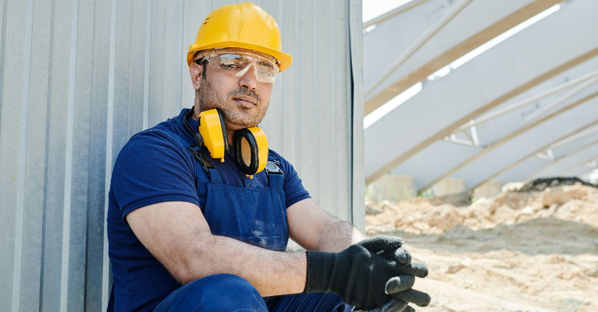 A male construction worker wearing safety gear sits at a construction site, showcasing standard industry protection.