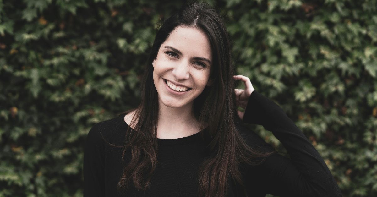 a smiling woman in a black top stands in front of a bush